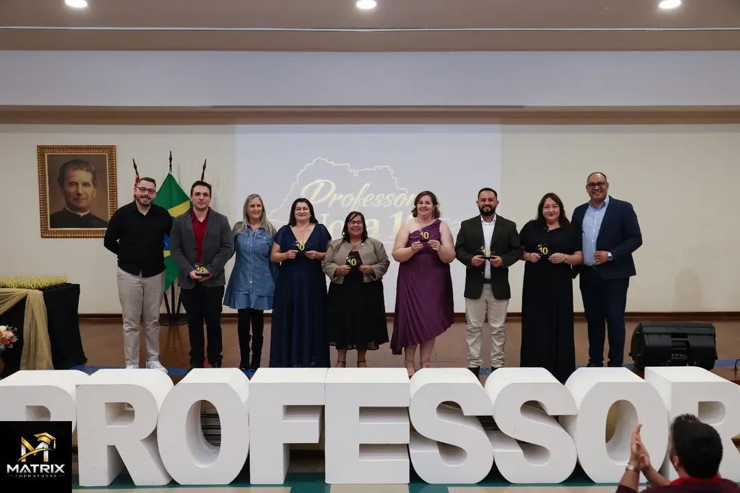 Professores da escola em pé no palco, segurando os troféus do Professor Nota 10, durante a cerimônia