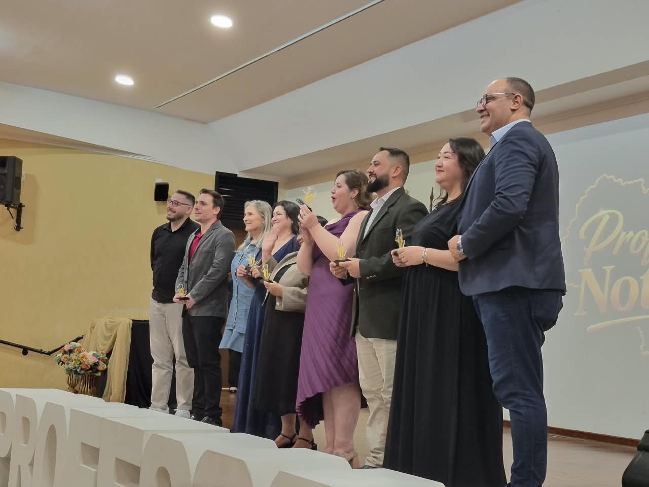 Professores premiados posando para foto ao lado do letreiro Professor Nota 10
